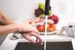 washing hands at sink with fruit behind